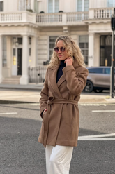 a lady in a brown wrap coat and a pair of white pants